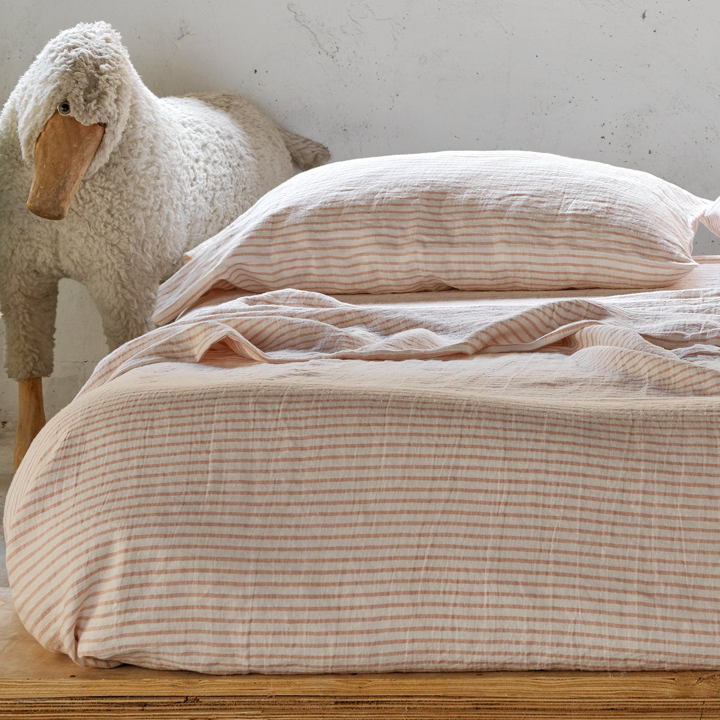 Cama de madera con amplio colchón vestido con lino rayado rosa y blanco. Lino marinero.