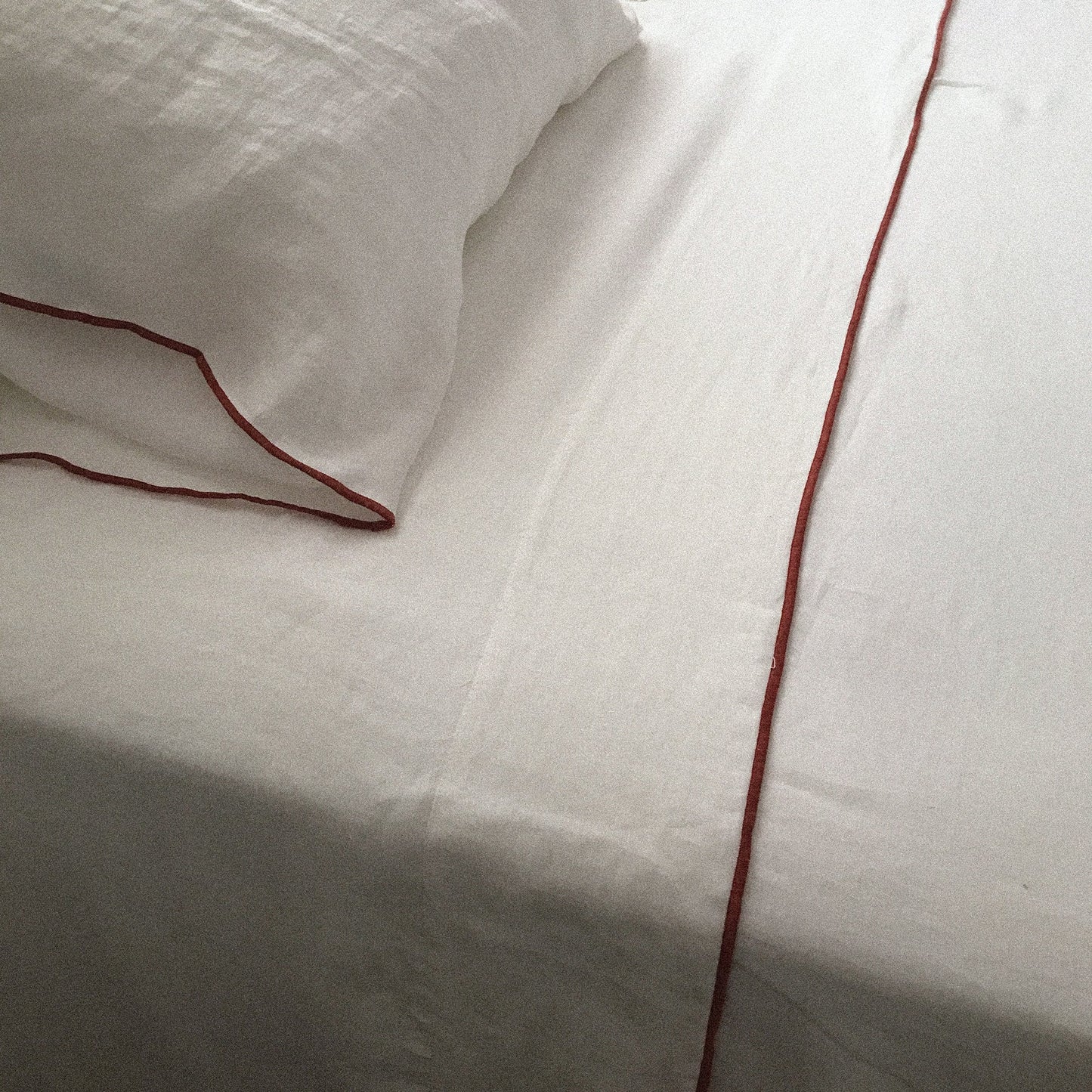 Juego de sábanas de lino blanco con repulgo coral.