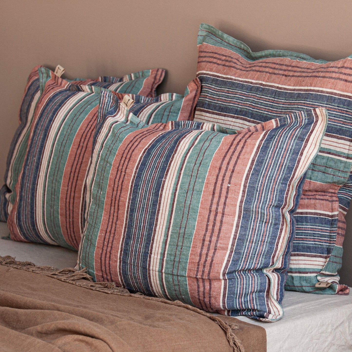 Grupo de cojines de lino rayado sobre colcha terracota.