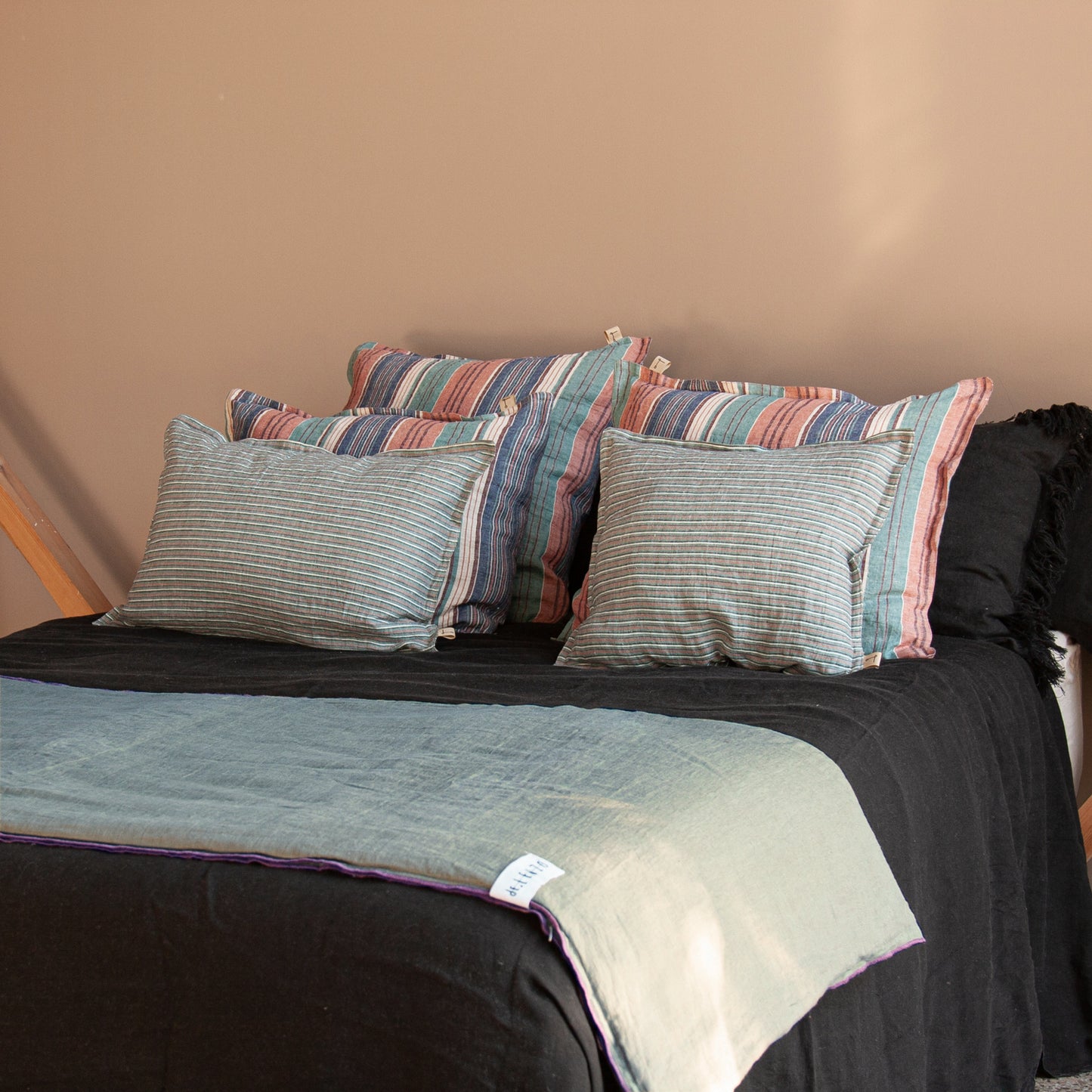 Conjunto de cojines a  rayas.Cojines de lino sobre sábana negra y pie de cama azul.