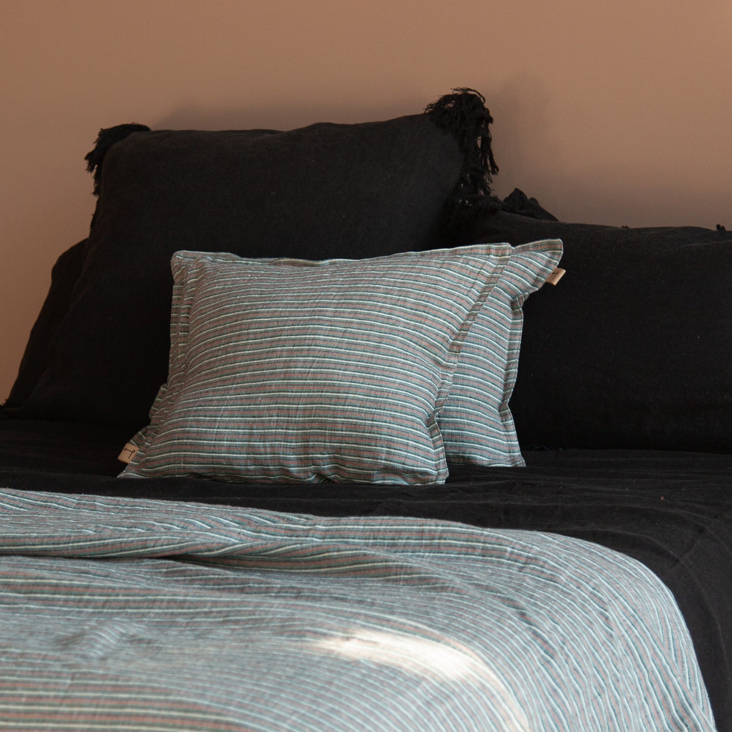 Cojín de lino con su pareja sobre cojines de lino negro desflecados. Plaid a juego.