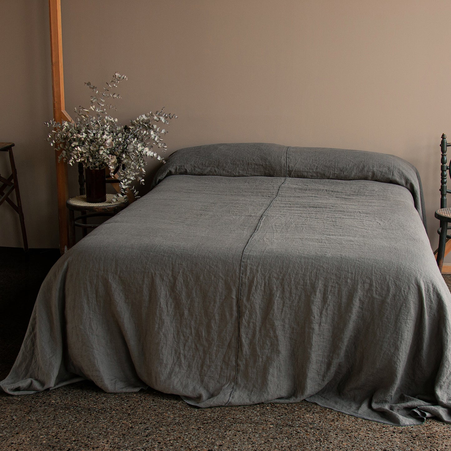 Colcha gris de lino y flores secas en silla antigua.