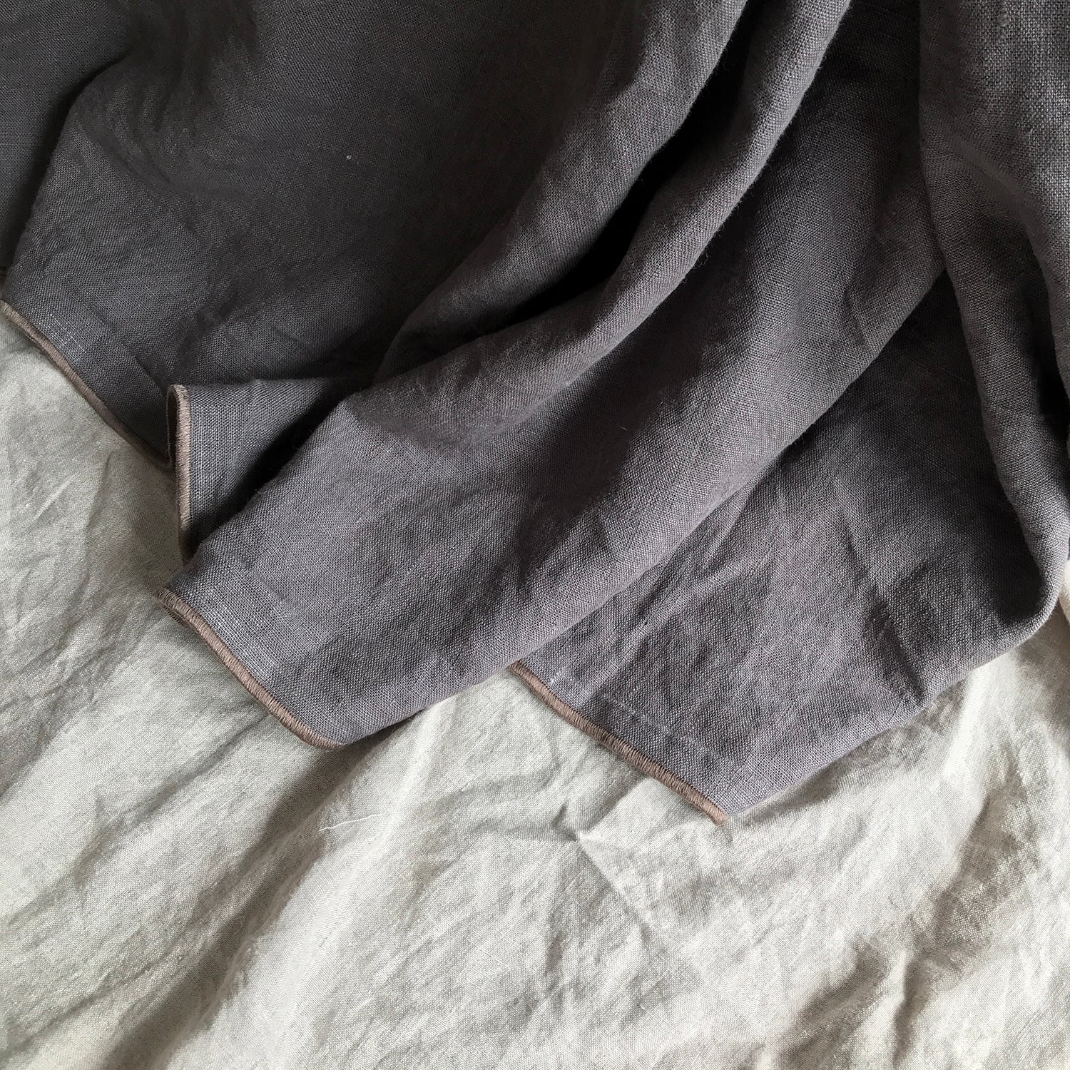 Plaid cubre sofá de lino gris con ribete marrón.