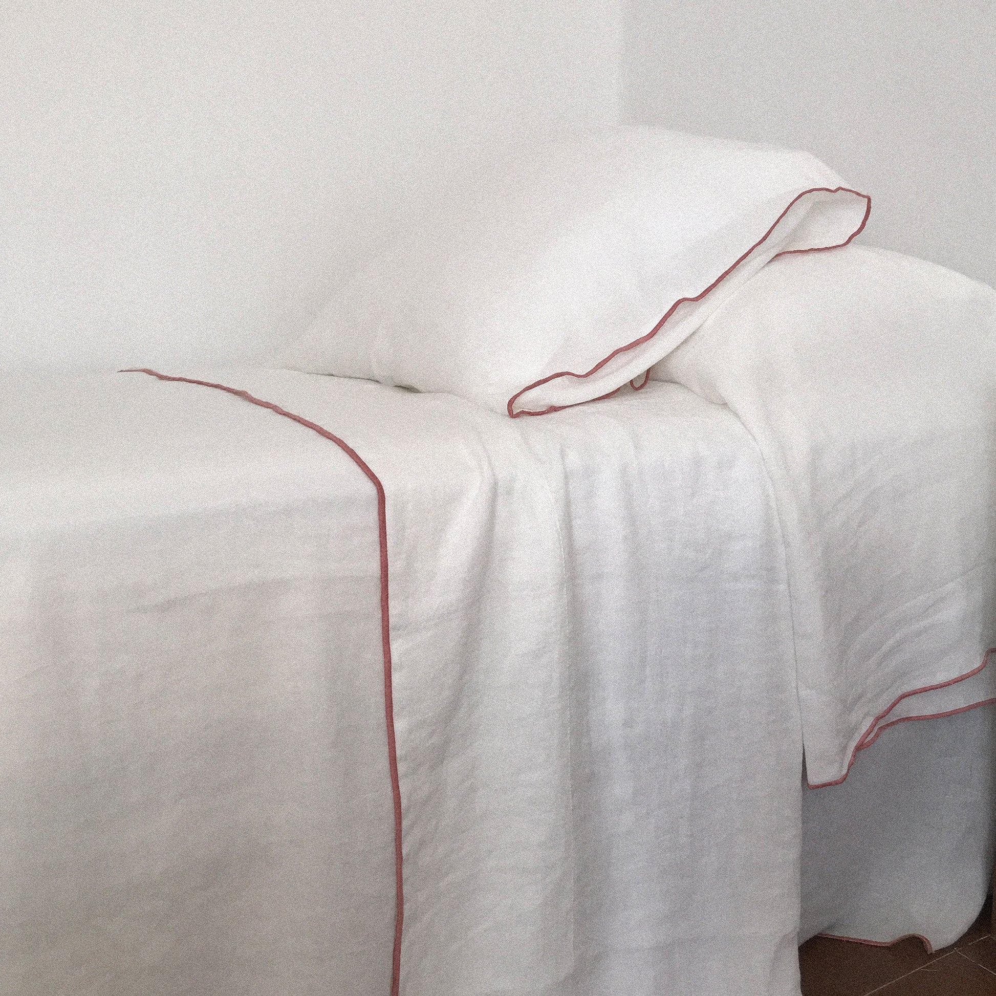 Sábanas de lino blanco con detalle de color burdeos.