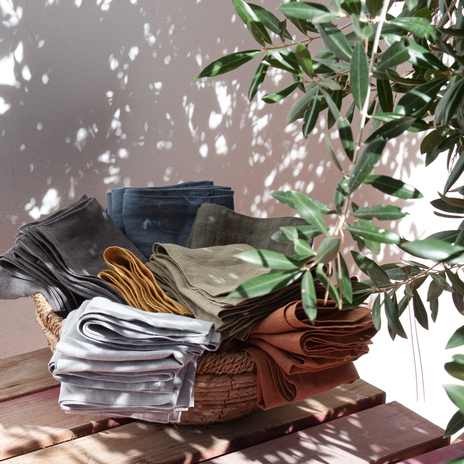 Servilletas de lino de colores en una cesta de mimbre con olivo en sombra