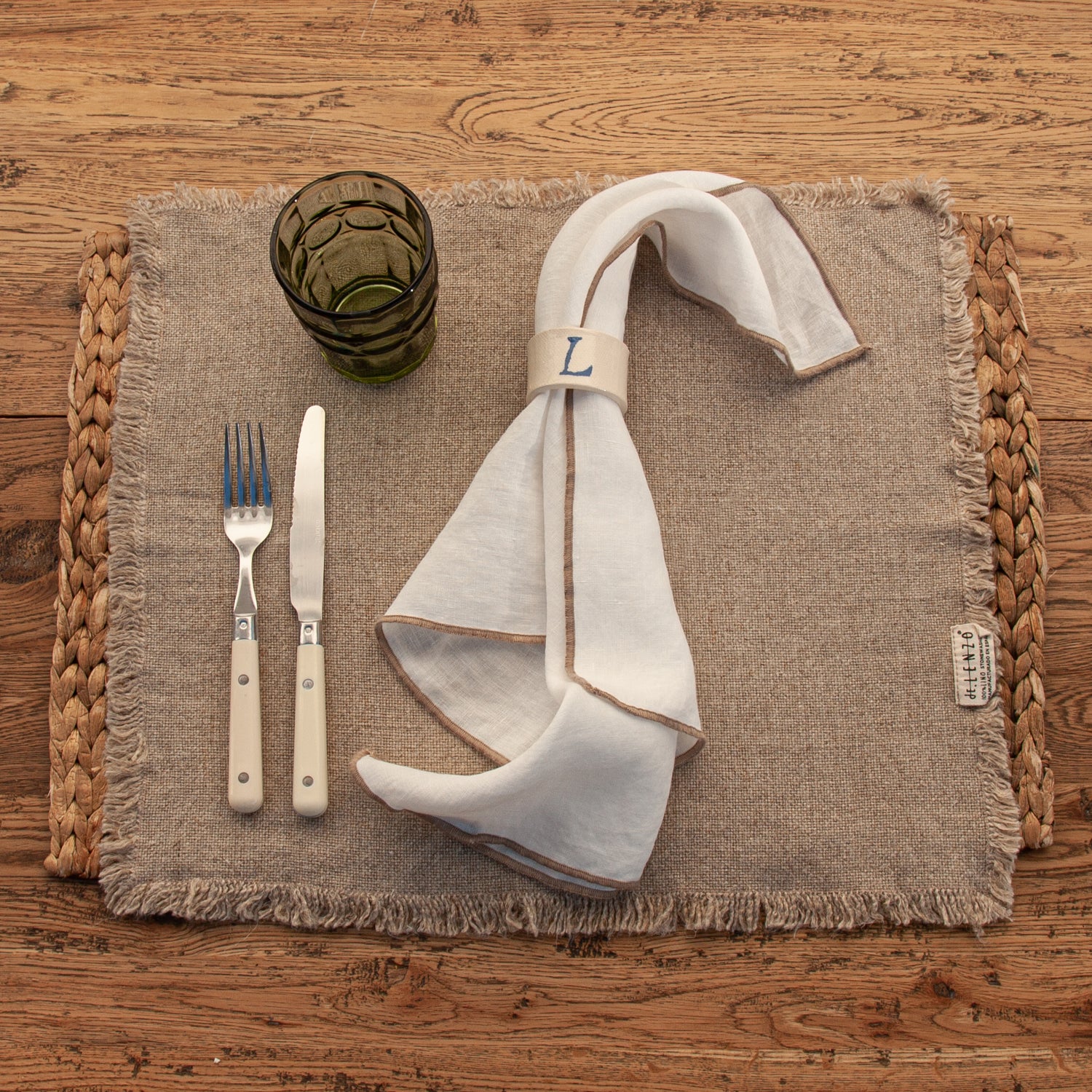 Servilleta de lino blanco con repulgo de color natural. Individual de lino Formentera con cubiertos y vaso de cristal verde.