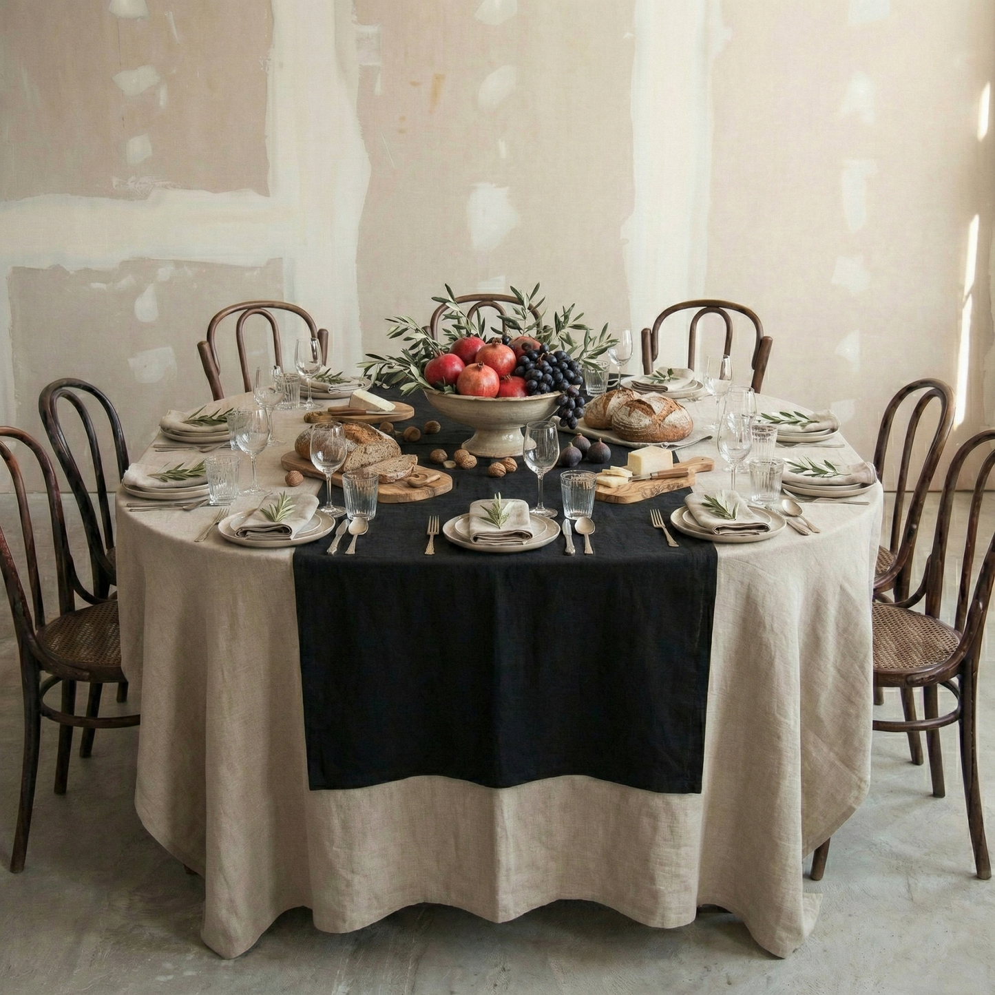 Mesa redonda con mantel de lino natura y camino negro.