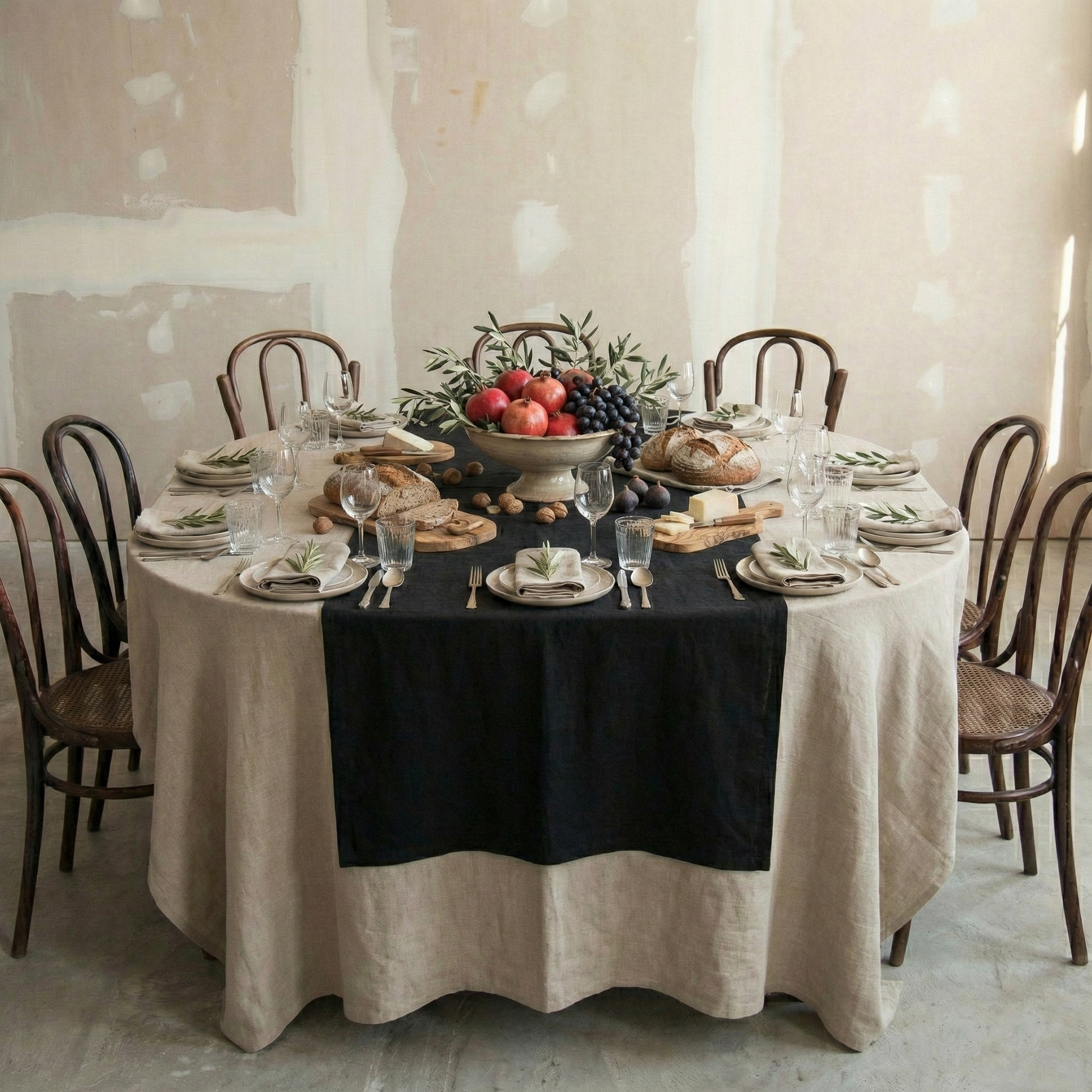 Mesa redonda con mantel de lino natura y camino negro.