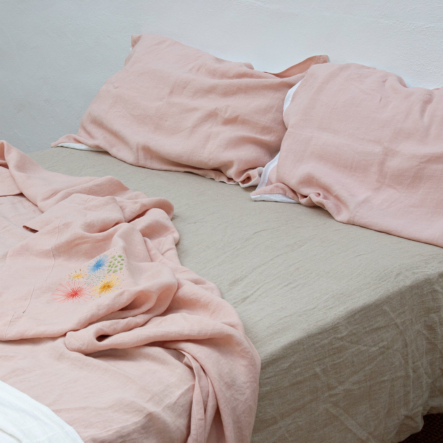 Sábanas rosas de lino bordadas con colores y bajera de lino natural.