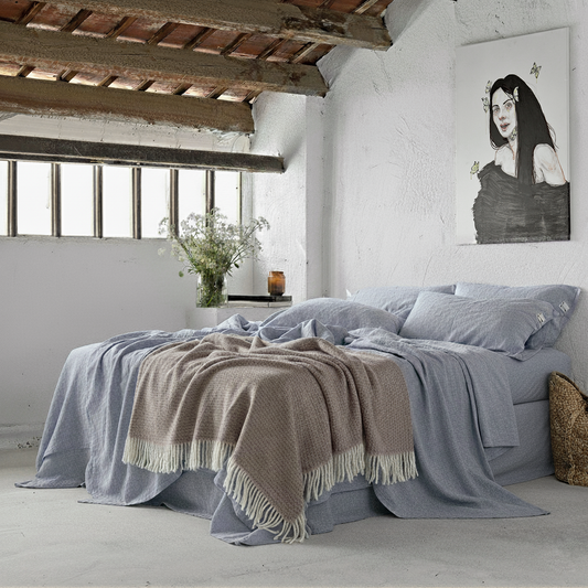 Juego de sábanas  de lino en una cama con paredes blancas encaladas con ventanas