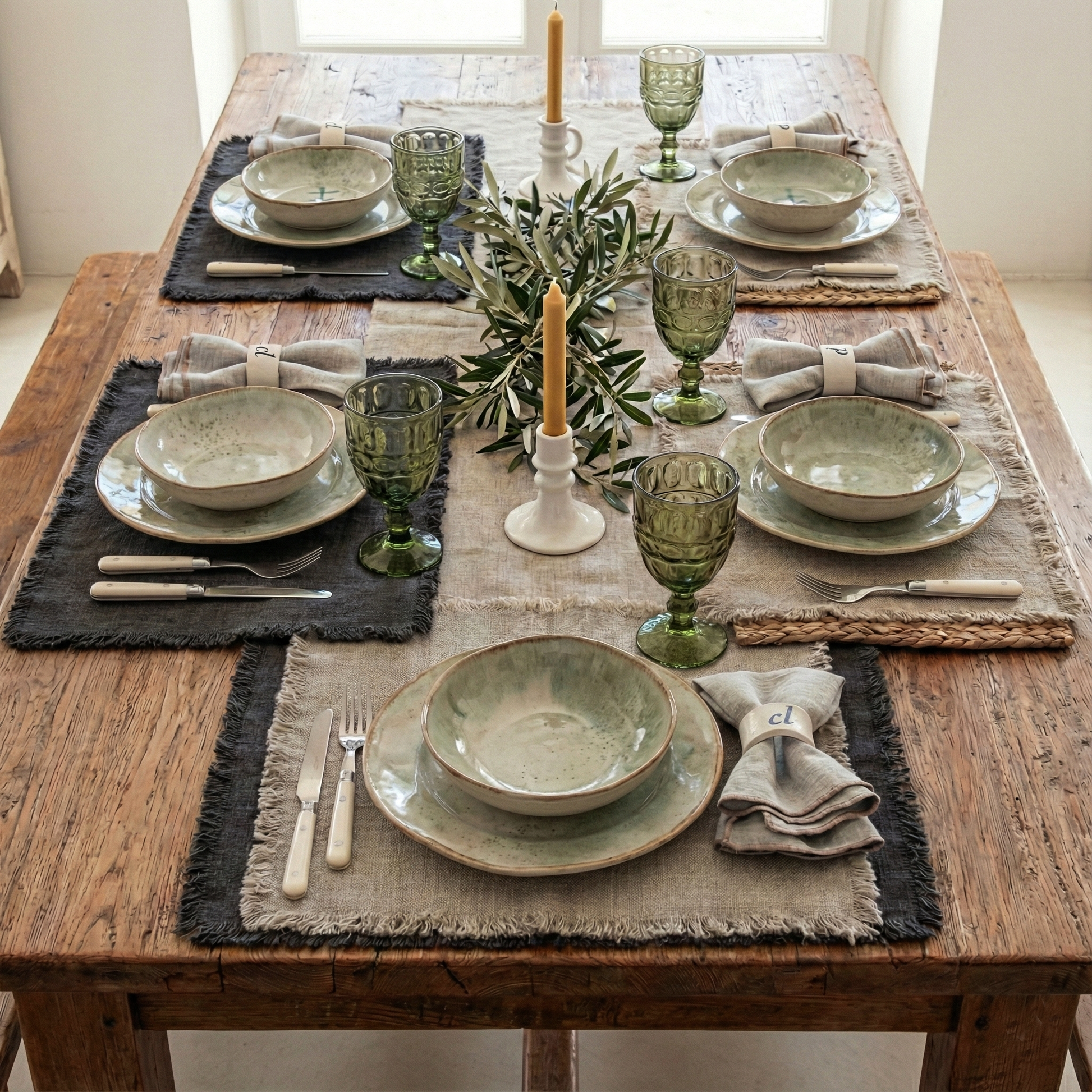 mesa con individuales de varios colores de lino desflecado. Copas de vidrio verdes.